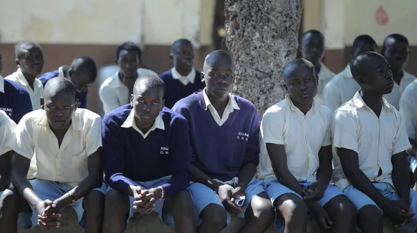 Kenia, Kisumu - 20 maja 2017: Grupa afrykańskich dzieci siedzi na ziemi. Chłopców i dziewcząt w mundurze spędzać czas na zewnątrz. Obrazek Stockowy