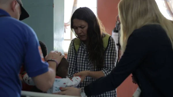 KENYA, KISUMU - MAY 20, 2017: Group of caucasian people holding little African childe on hands. Volunteers in hospital. Stock Image