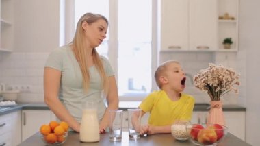 Güzel beyaz Anne oğlunu mutfakta masada eğlenmeyi. Aile mutfak eğleniyor. Kadın uzun beyaz saçlı, sevimli oğlu sarı gömlekli. Modern mutfak. Oturma