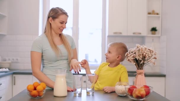 Hermosa madre caucásica jugando con su hijo en la cocina en la mesa. Familia divirtiéndose en la cocina. Camisa brillante y colorida. Hermosa luz moderna cocina. Camisas brillantes . — Vídeo de stock