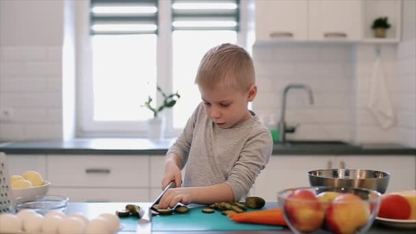 Little beautiful caucasian boy with big blue eyes cooking in the bright kitchen. — Stock Video