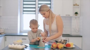 Anne oğlu peynir ovmak için öğretir. Genç güzel bir anne ile beyaz gömlek ve beyaz mutfak aşçı şirin oğlu.