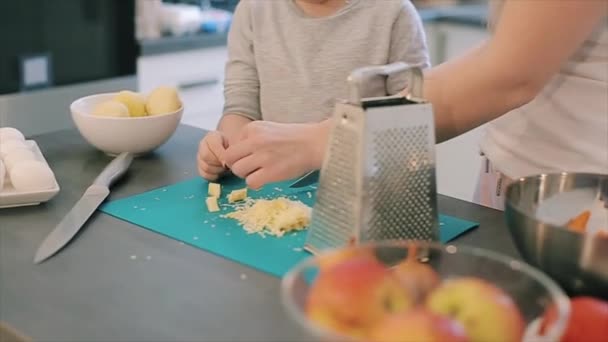 Mor skär ost och ge till sin son på köket. Ung mamma och söt vacker son med stora ögon matlagning toghether. Familjen att göra pizza. — Stockvideo