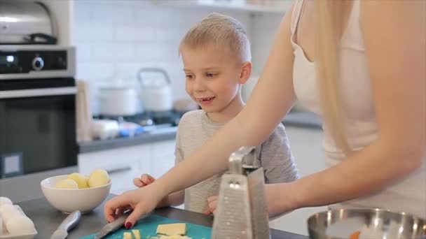 Moeder snijden kaas en geven aan haar zoon over de keuken. Jonge moeder en leuke mooie zoon met grote ogen toghether koken. Familie pizza maken. — Stockvideo