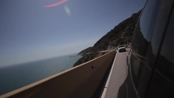 Feche o lado de cima do carro e leve na estrada. Céu azul e mar azul. A conduzir um carro na estrada da montanha. O carro anda em serpentina. Mar Mediterrâneo nas proximidades. Visão traseira do carro — Vídeo de Stock