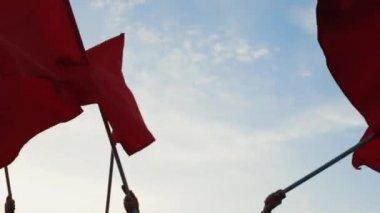 Bir grup kişiye karşı mavi gökyüzü kırmızı bayraklar sallayarak elleri