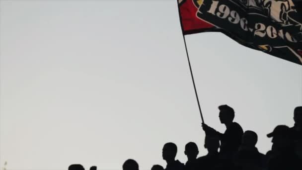 Bobruisk, Biélorussie - AVRIL 2018 : Silhouettes de supporters de football agitant le drapeau contre le ciel bleu. Mouvement lent . — Video