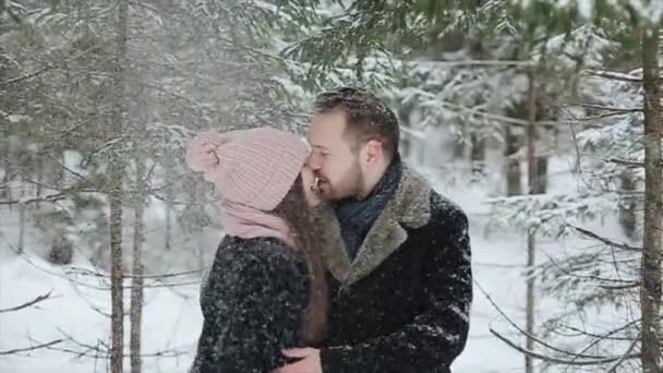 Unga vackra kaukasiska par kyssar under en snö i en vinter skog. Fashionabla millennials har roligt tillsammans. Uppriktig bilder av unga par i skogen. Slow motion. — Stockvideo