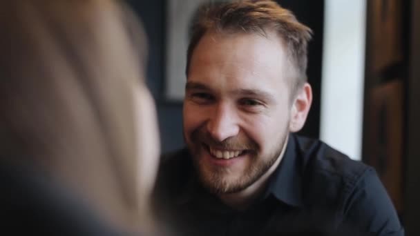 Primer plano retrato de un joven feliz está bebiendo café, hablando y sonriendo con su novia mientras está sentada en el café. Vista desde encima del hombro . — Vídeos de Stock