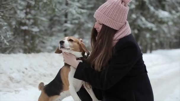 Szczęśliwy piękną, młodą kobietę w różowy kapelusz jej pieszczoty pies rasy beagle w zimowy dzień. Przyjaźń, zwierzęta domowe i ludzi. Szczere i autentyczne nagrania. — Wideo stockowe