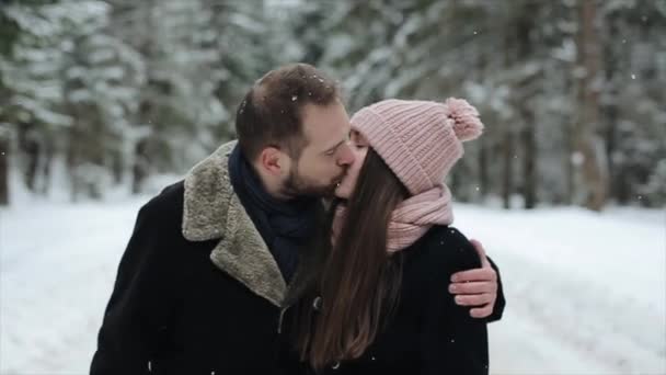 Jovem casal atraente andando ebeijando em uma floresta de inverno sob neve pesada. Movimento lento . — Vídeo de Stock