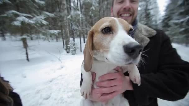 Cute young hipster couple having fun in winter park with their dog on a bright day and smiling. Man and woman playing with beagle. Slow motion, — Stock Video