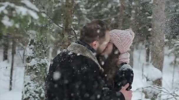 Junge schöne kaukasische Paar küsst sich unter einem Schnee in einem Winterwald. modische Millennials, die zusammen Spaß haben. Freimütige Aufnahmen eines jungen Paares im Wald. Zeitlupe. — Stockvideo