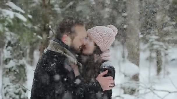 Casal caucasiano bonito jovem que se beija abaixo de uma neve em uma floresta de inverno. Millennials na moda se divertindo toghether. Imagens sinceras de um jovem casal na floresta. Movimento lento . — Vídeo de Stock