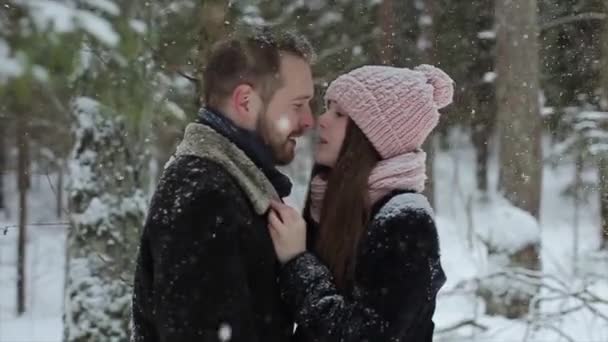 Young beautiful caucasian couple kissing under a snow in a winter forest. Fashionable millennials having fun toghether. Candid footage of young couple in forest. Slow motion. — Stock Video