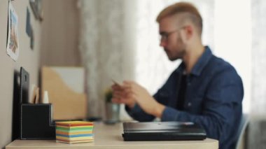 Gözlüklü şık saç kesimi ile genç erkek öğrenci notları etiket Resepsiyon Masa dizüstü bilgisayar ve günlüğü üzerinde yapar. Eğitim ve insan kavramı.