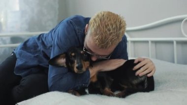 Yatakta köpek dachshund oynamaktan neşeli şık delikanlı. İnsan ve köpek having fun.