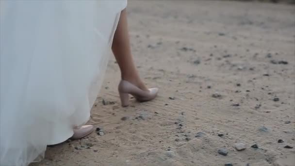 De voeten van de bruid in de schoenen lopen in het zand. — Stockvideo