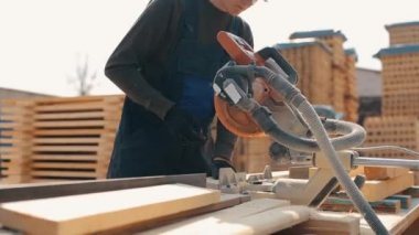 Ahşap kesme makinesi kullanarak inşaat gözlükleri ve üniforma giyen genç bir marangoz işçisi yakın. adam ahşap plakalar keser.