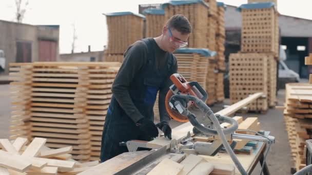 Ξυλουργός εργαζόμενος φορώντας γυαλιά κατασκευής με μηχανή κοπής ξύλου. άνθρωπος κόβει ξύλινες σανίδες. — Αρχείο Βίντεο