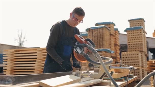 Close up de um jovem carpinteiro usando óculos de construção e uniforme usando máquina de corte de madeira. homem corta tábuas de madeira. Movimento lento . — Vídeo de Stock