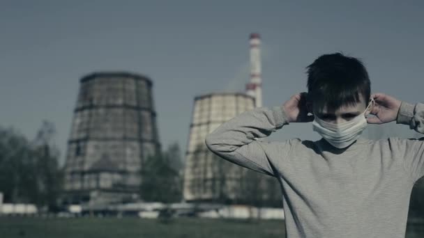 Junge setzte Verschmutzungsmaske gegen Fabrikschornsteine und blickte in die Kamera. Luftverschmutzungskonzept — Stockvideo