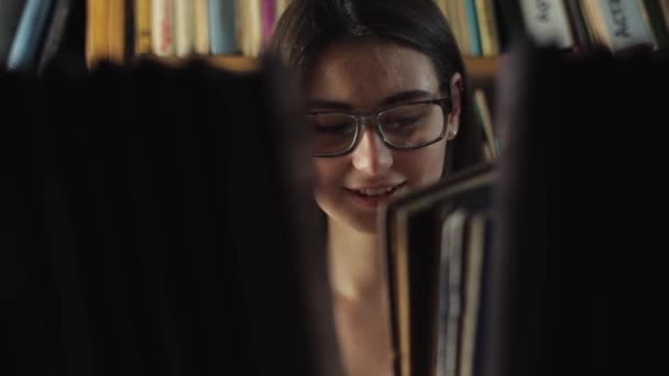 Atractiva joven buscando un libro de una estantería en la biblioteca — Vídeo de stock