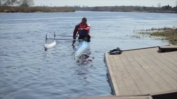 Nehirde bir kano içinde atlet kürek. Adam iskeleye yaklaşıyor. Kürek, Kano, kürek çekme. Eğitim. Kayak. Köprüye karşı yelken açman. — Stok video