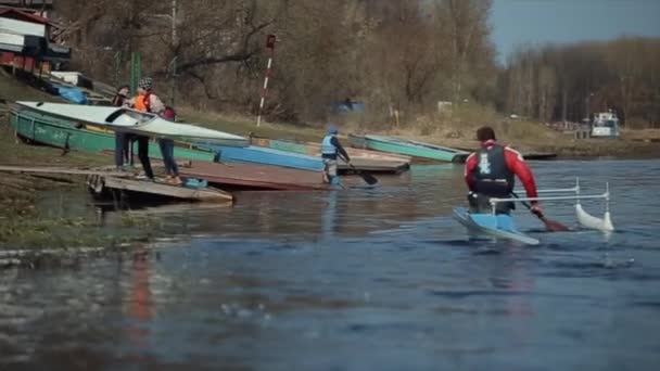 Бобруйськ, Білорусь-11 травня 2019: спортсмен веслування на річці в каное. Людина, що наближається до дока. Веслування, Каноє, дитячий. Навчання. Каякінг. діти з каное на задньому плані — стокове відео