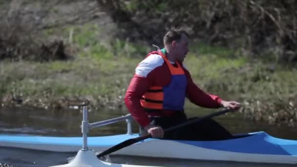 Bobruisk, Belarus - 11 May 2019: Close up portrait of Athlete rowing on the river in a canoe. Rowing, canoeing, paddling. Training. Kayaking. Man sailing against the bridge. Tracking shot — Stock Video