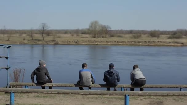 Bobruisk, Bielorussia - 11 maggio 2019: Quattro ragazzi seduti su una panchina di legno contro il fiume . — Video Stock