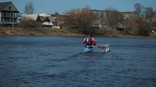 Bobruisk, Belarus - 11 May 2019: Rear view of Athlete rowing on the river in a canoe. Rowing, canoeing, paddling. Training. Kayaking. Man guy is rowing against the background of the houses of the — Stock Video