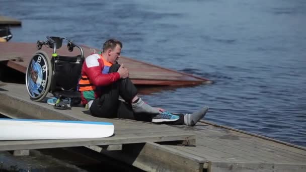 Bobruisk, Vitryssland-11 maj 2019: idrottaren är handikappad sitter på bryggan och bär sneakers efter träning på kanot. Rodd, Kanotpaddling, paddling. Utbildning. Kajakpaddling. — Stockvideo