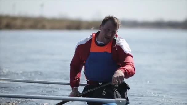 Nahaufnahme Porträt eines Athleten, der im Kanu auf dem Fluss rudert. Rudern, Kanufahren, Paddeln. Ausbildung. Kajakfahren. Mann fährt gegen Brücke. — Stockvideo