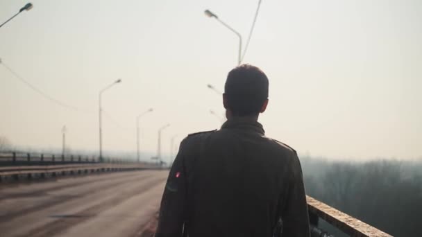 Ένας νέος άντρας που περπατάει στη γέφυρα. Τα αμάξια πάνε στο δρόμο. Πρωί και ομίχλη. Άνοιξη. — Αρχείο Βίντεο