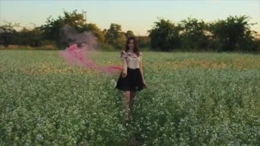 Alanında pembe bir sis bombası ile etek genç çekici esmer kız. Gün batımına karşı dumanla eğlenen ve dumanla dönen kız.