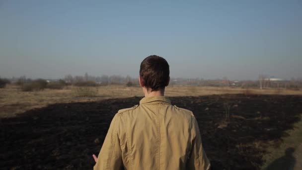 Hombre se para en el fondo de la hierba quemada y agarra su cabeza. Lágrimas de pelo en la cabeza y lamenta indignado enojado debido a la destrucción de la naturaleza — Vídeo de stock