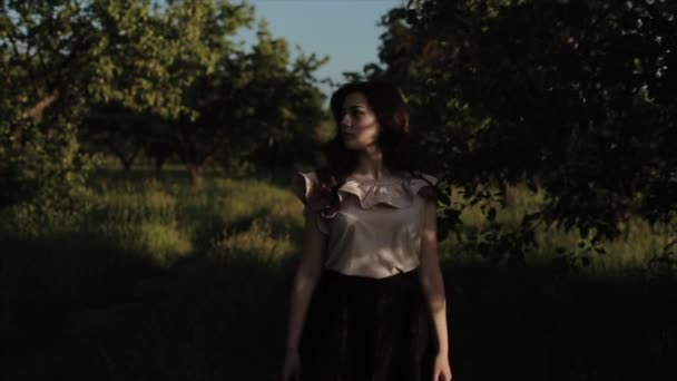 Portret van een charmant mooi brunette meisje met een schattige glimlach met natuurlijke make-up in de zomer elegante kleren tegen een groene bomen. Gelukkig elegant meisje in bos. bomen schaduw op haar gezicht — Stockvideo