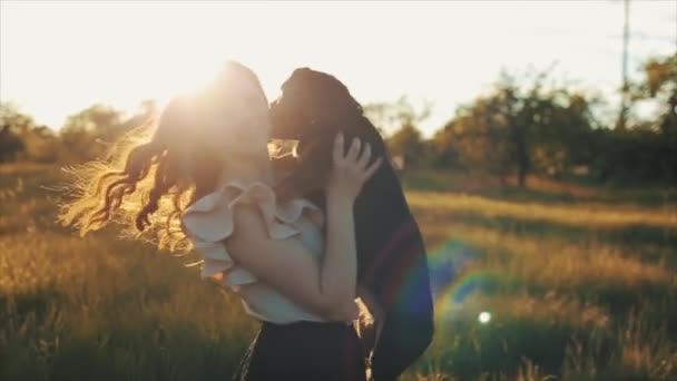 Trendig vacker flicka i snygg sommarklänning och svart vågigt hår med hundtax i fält med blommor i solljus, gräs vid solnedgången. Kvinnan ler, skrattar och virvlar med hunden — Stockvideo