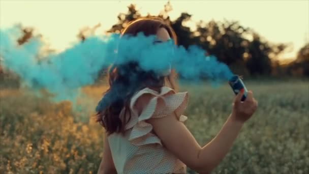 Молодая привлекательная брюнетка в юбке с голубой дымовой шашкой на поле. Девушка веселится смеясь наслаждаясь и кружась от дыма против заката . — стоковое видео