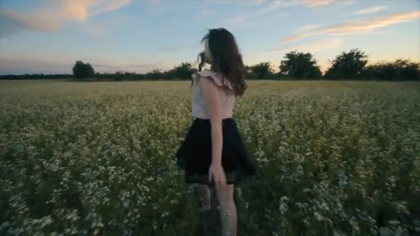 검은 치마에 물결 모양의 머리를 가진 예쁜 젊은 갈색 머리 소녀의 백뷰는 꽃밭에서 실행됩니다. 후면 보기. 슬로우 모션 — 비디오