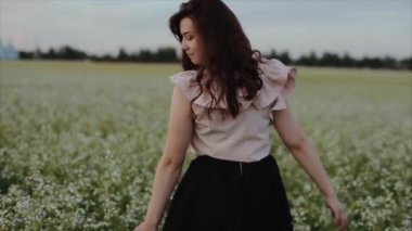 Siyah etekli güzel genç esmer kız sahada yürüyor. arkadan görüntüleyin. Omzunun üzerinden döner ve kameraya bakar. Yavaş çekim