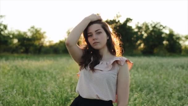 Hermosa chica joven despreocupada con pelo largo y rizado sobre fondo de paisaje de campo de trigo de flor. El sol del atardecer brilla por detrás en el cabello. Atractivo morena disfrutando y respirando puesta de sol — Vídeo de stock