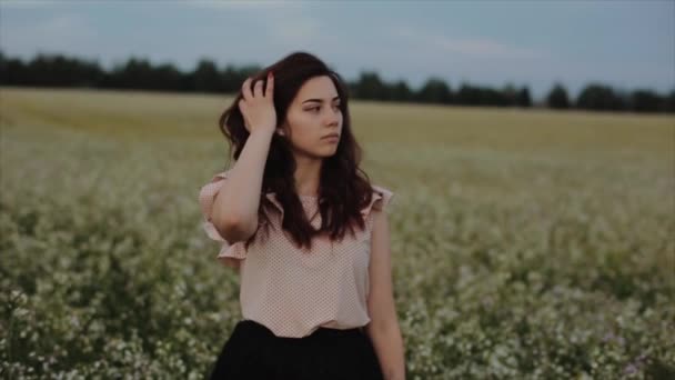 Mooie jonge zorgeloze meisje met lang krullend haar over bloem tarwe veld landschap achtergrond. De zonsondergang zon schijnt van achteren in het haar. Aantreive brunette genieten en ademen zonsondergang — Stockvideo