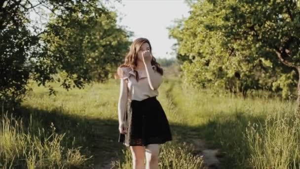 Krásná mladá žena v černé sukni s vlnitými vlasy v cestě v lese, úsměvy a skvrnami. — Stock video