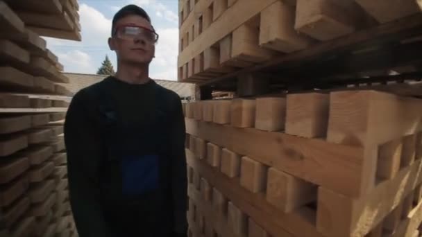 Um jovem trabalhador de uniforme caminha entre paletes de madeira em armazém ao ar livre distribuição. Movimento lento — Vídeo de Stock