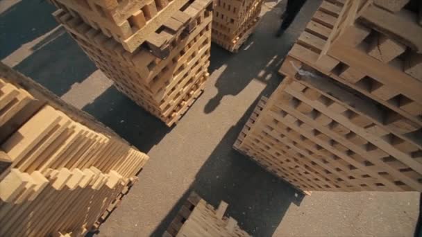 Un joven trabajador en uniforme camina entre paletas de madera en almacén de distribución al aire libre. En cámara lenta. vista desde arriba — Vídeo de stock