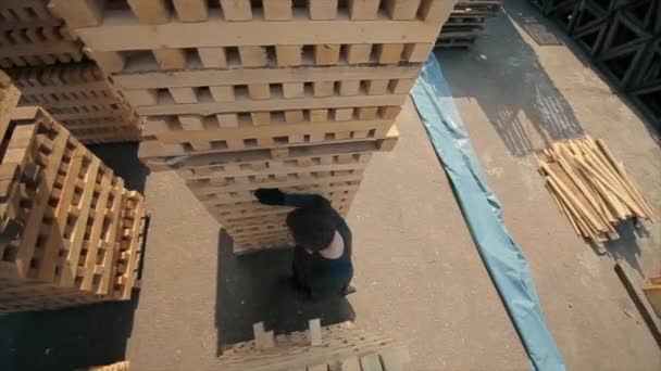 Un joven trabajador en uniforme camina entre paletas de madera en almacén de distribución al aire libre. En cámara lenta. vista desde arriba — Vídeos de Stock