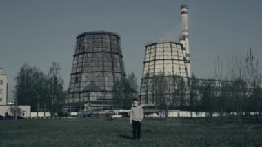 Genç çocuk fabrika bacalarının önünde yürüyor. Hava kirliliği. Arka planda genç adam witn bitki yakın portresi.