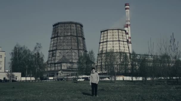 Jonge jongen wandelingen Infront van de fabriek schoorstenen. Luchtverontreiniging. Close-up portret van jonge Guy Witn plant op achtergrond. — Stockvideo
